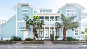 Une maison à deux étages avec un porche, de grandes fenêtres et des palmiers.