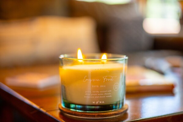 A lit candle in a glass holder with text indicating it is 'Evergreen Forest' and established in 2014.