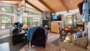 A cozy cabin interior with a stone fireplace, leather furniture, and a television.