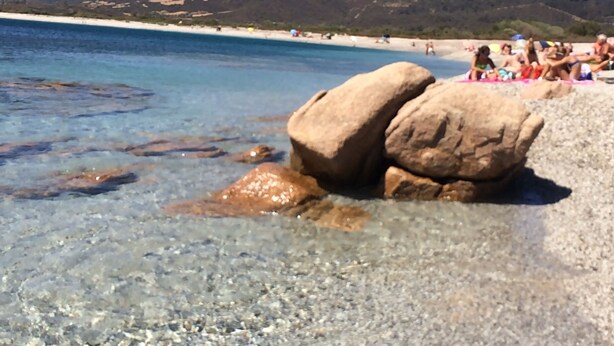 A beach with clear water, large rocks, and people in the background. - Charming apartment on the mountainside near the sea (Villaputzu)
