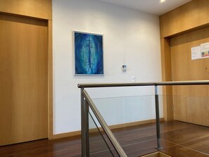 A modern hotel lobby with wooden paneling, a glass railing, and a blue abstract painting on the wall.