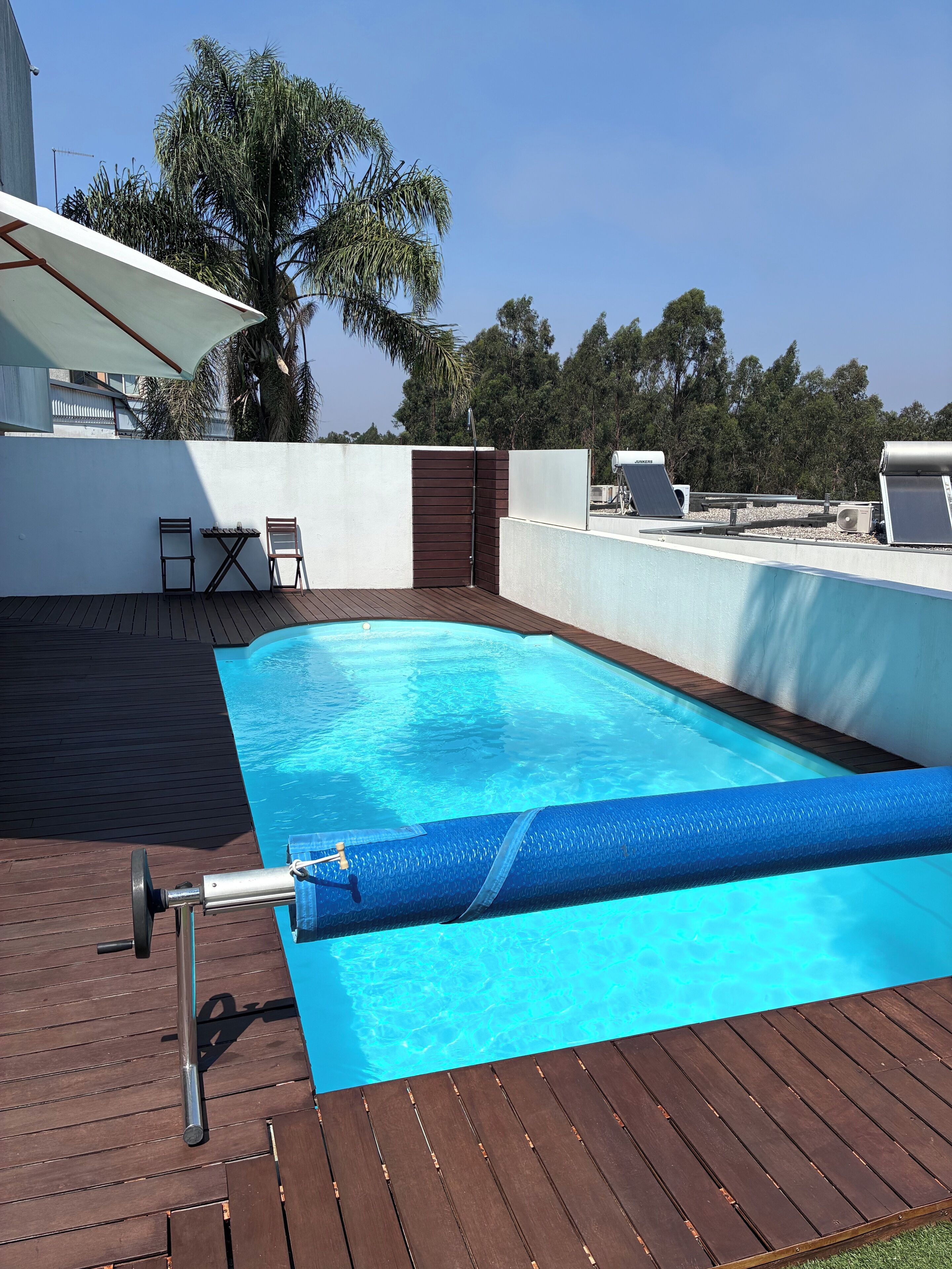 A rooftop pool with a wooden deck, two chairs, and a table.