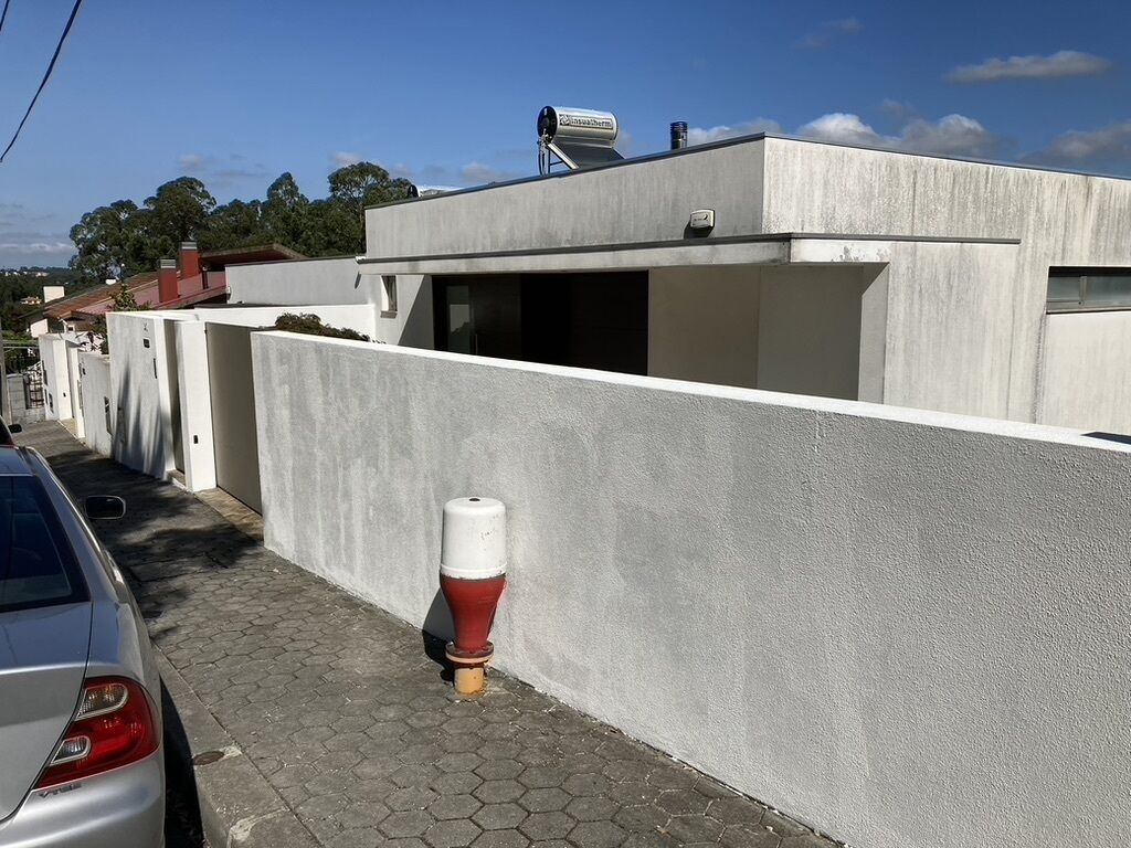 Un bâtiment moderne avec une façade en béton, une antenne parabolique sur le toit et un poteau blanc sur le trottoir.