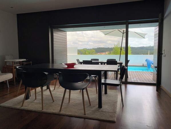 Un espace repas moderne avec une table et des chaises, une vue sur une piscine et une grande porte-fenêtre coulissante donnant sur une terrasse extérieure.