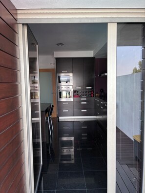 Una cocina moderna con electrodomésticos integrados, una puerta corrediza de vidrio que da a un balcón y vistas al exterior.