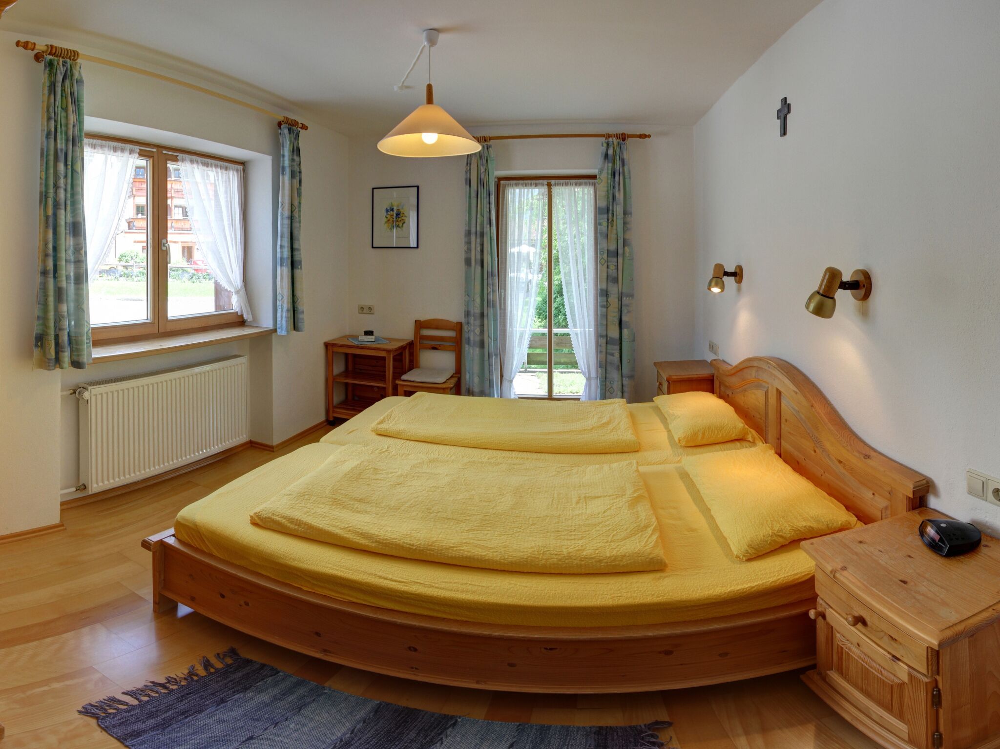 A bedroom with a large bed, a wooden nightstand, a chair, a desk, and a window with curtains.