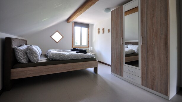 Ein Schlafzimmer mit Schlafbox, Holzbalken, großem Kleiderschrank und Fenster mit Aussicht.