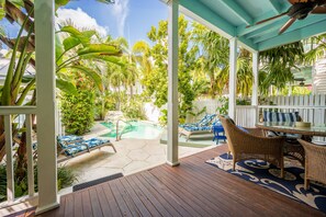 A covered outdoor area with a pool, lounge chairs, and a table with chairs.