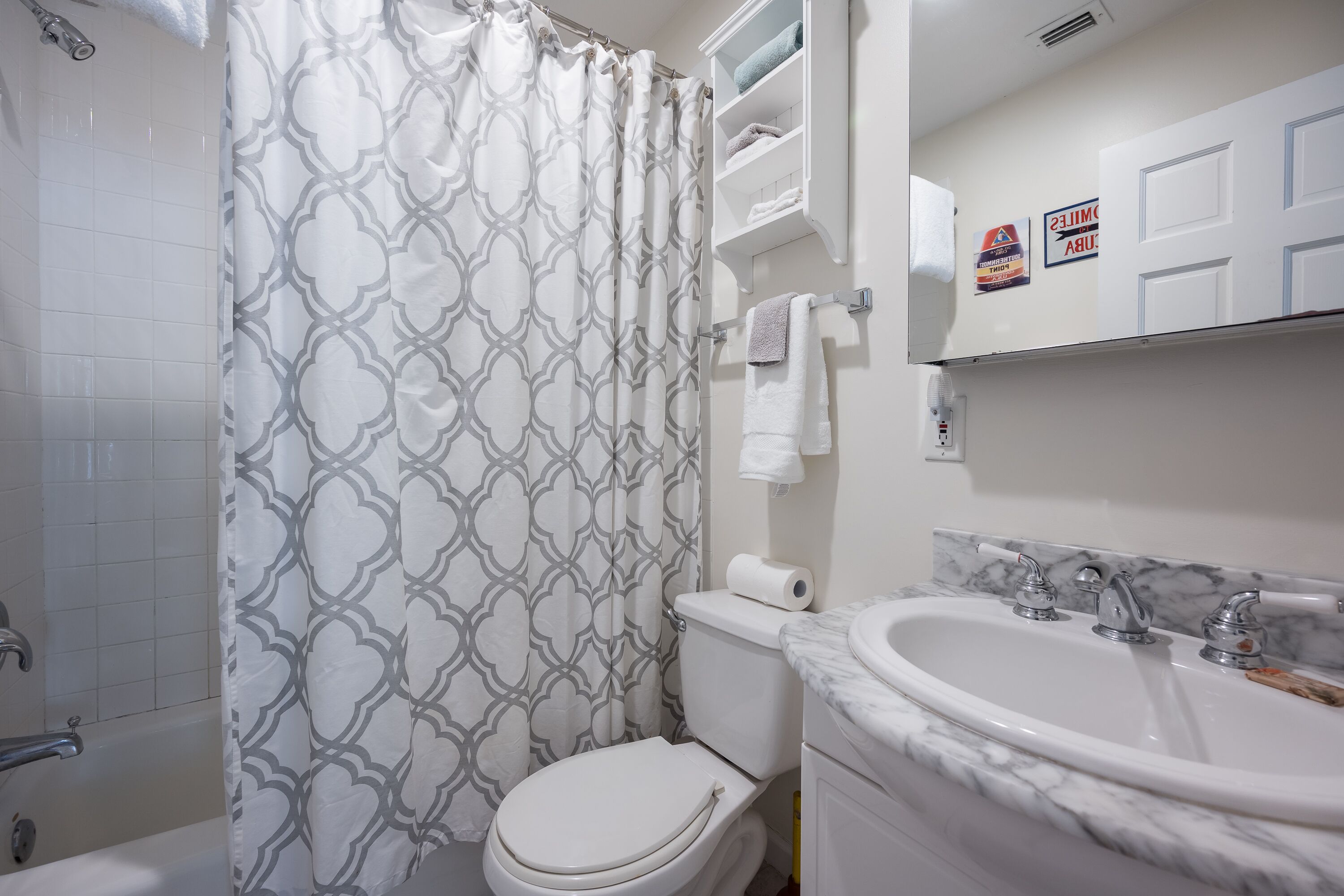 A bathroom with a patterned shower curtain, a toilet, a sink with a marble countertop, and a towel rack.