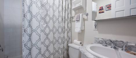 A bathroom with a patterned shower curtain, a toilet, a sink with a marble countertop, and a towel rack.