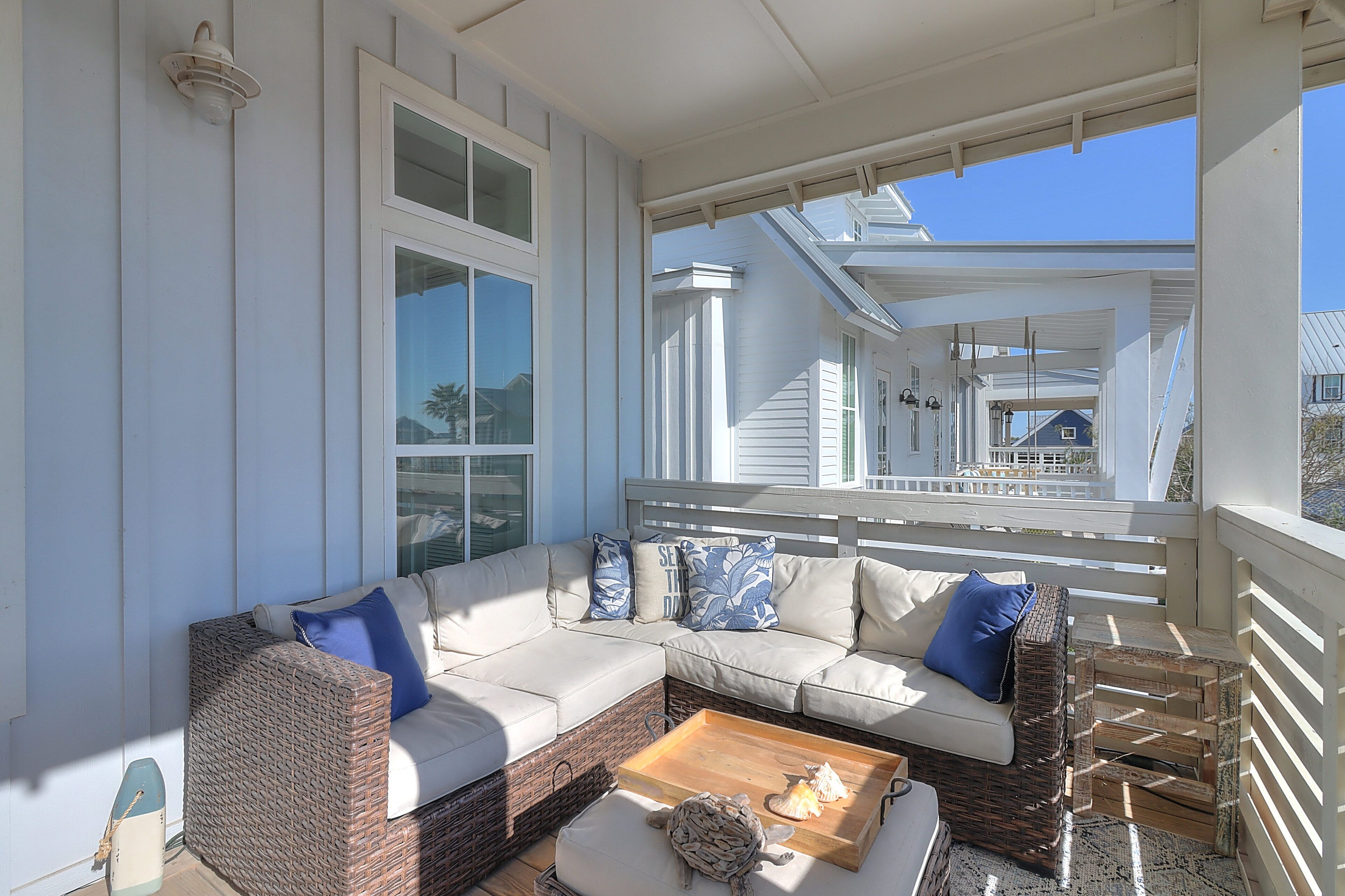 A covered porch with a wicker sofa, a wooden coffee table, and a small table with decorative items.