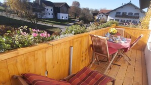 A wooden deck with a cushioned bench and a table set for dining, overlooking a residential area. - Farmhouse vacation rental, 55 square meters, sleeps up to 4, ideal for families (Obing)