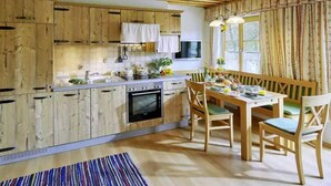 A kitchen with wooden cabinets, a dining table with chairs, and a window with curtains. - Farmhouse vacation rental, 55 square meters, sleeps up to 4, ideal for families (Obing)