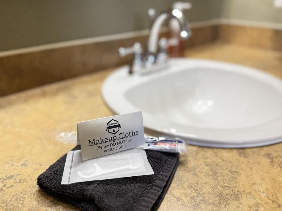 A bathroom sink with a sign instructing not to use white cloths, a black towel, and makeup cloths on the counter.