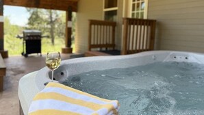 A hot tub with a glass of wine and a towel, wooden deck, and a house in the background.