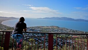 Une personne qui contemple un paysage côtier, avec vue sur la mer et les montagnes au loin.