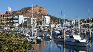 Un port de plaisance avec des bateaux amarrés, des bâtiments en arrière-plan et une colline surmontée d’une structure en forme de dôme.
