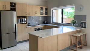 Une cuisine moderne avec des meubles en bois, un réfrigérateur en acier inoxydable, un four encastré et un grand îlot central doté d’un évier.