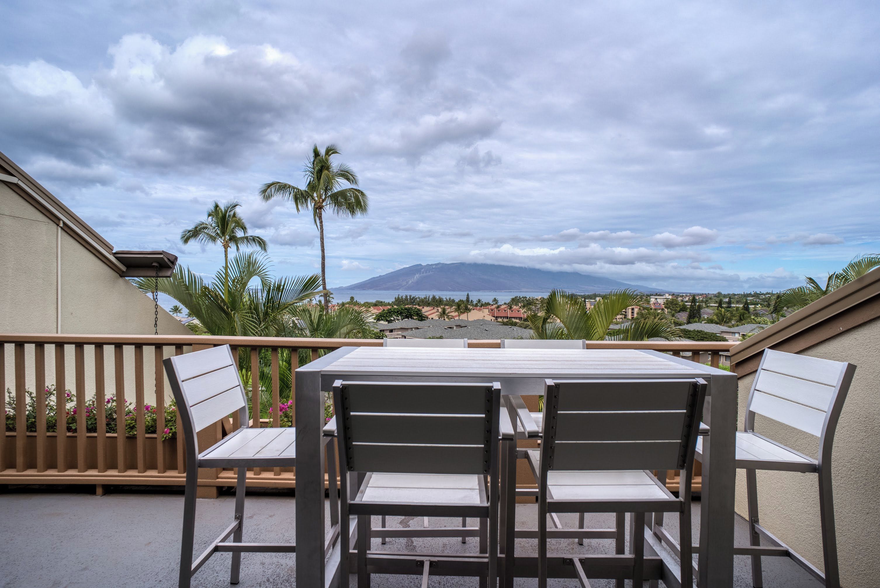 A balcony with a table and chairs, overlooking a scenic view of a mountain and a town.
