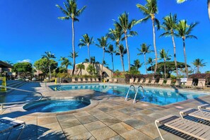 A pool area with lounge chairs, palm trees, and a clear blue sky.