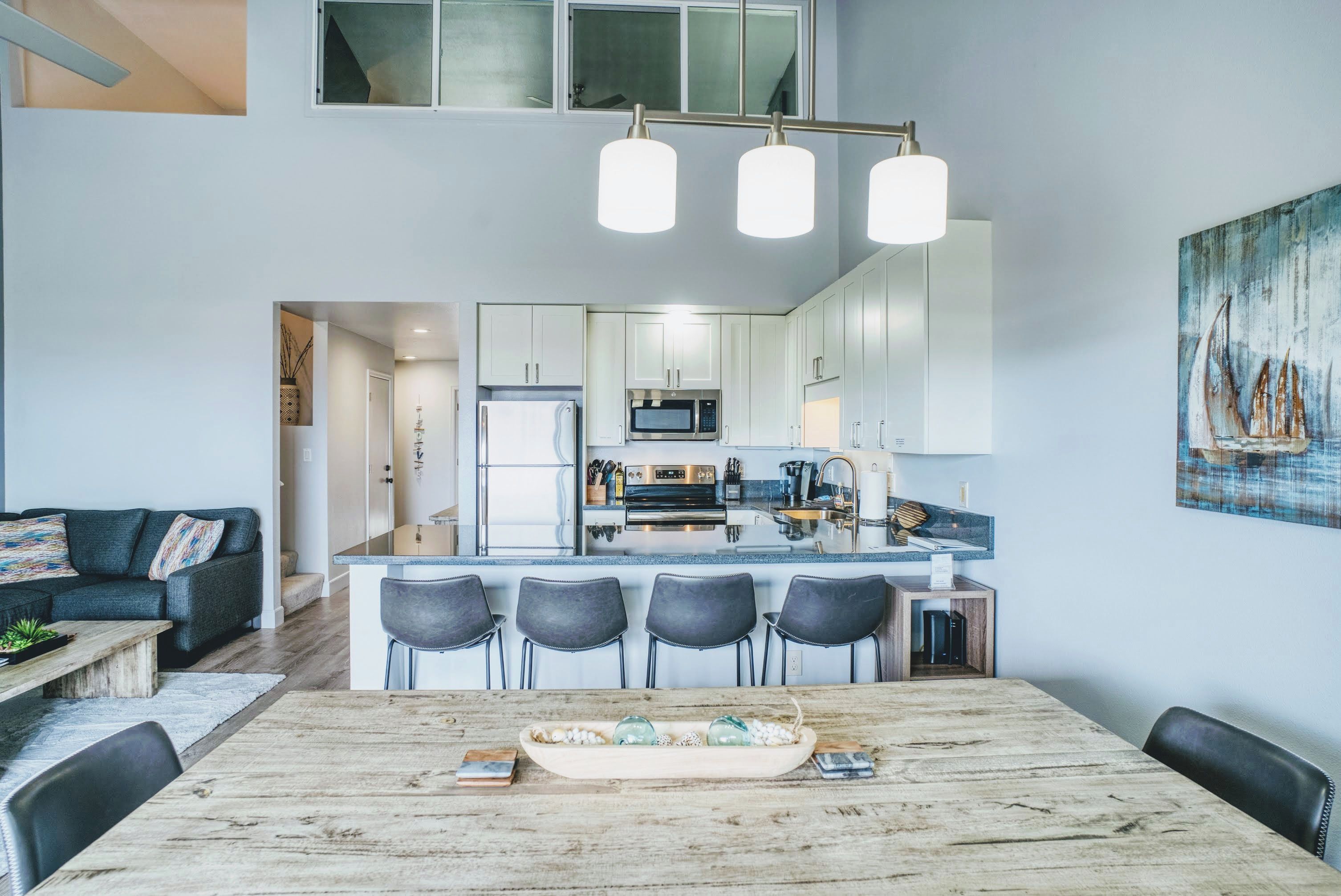 Een moderne keuken met witte kasten, een centraal eiland met barstoelen en een eethoek met een houten tafel.