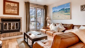 Een woonkamer met een open haard, een leren bank en een groot raam met gordijnen.