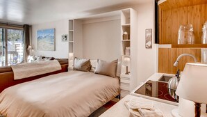 Hotelkamer met een groot bed, een ingebouwd bureau met een wastafel, een houten plank met decoratieve items, en een raam met uitzicht op de omgeving.