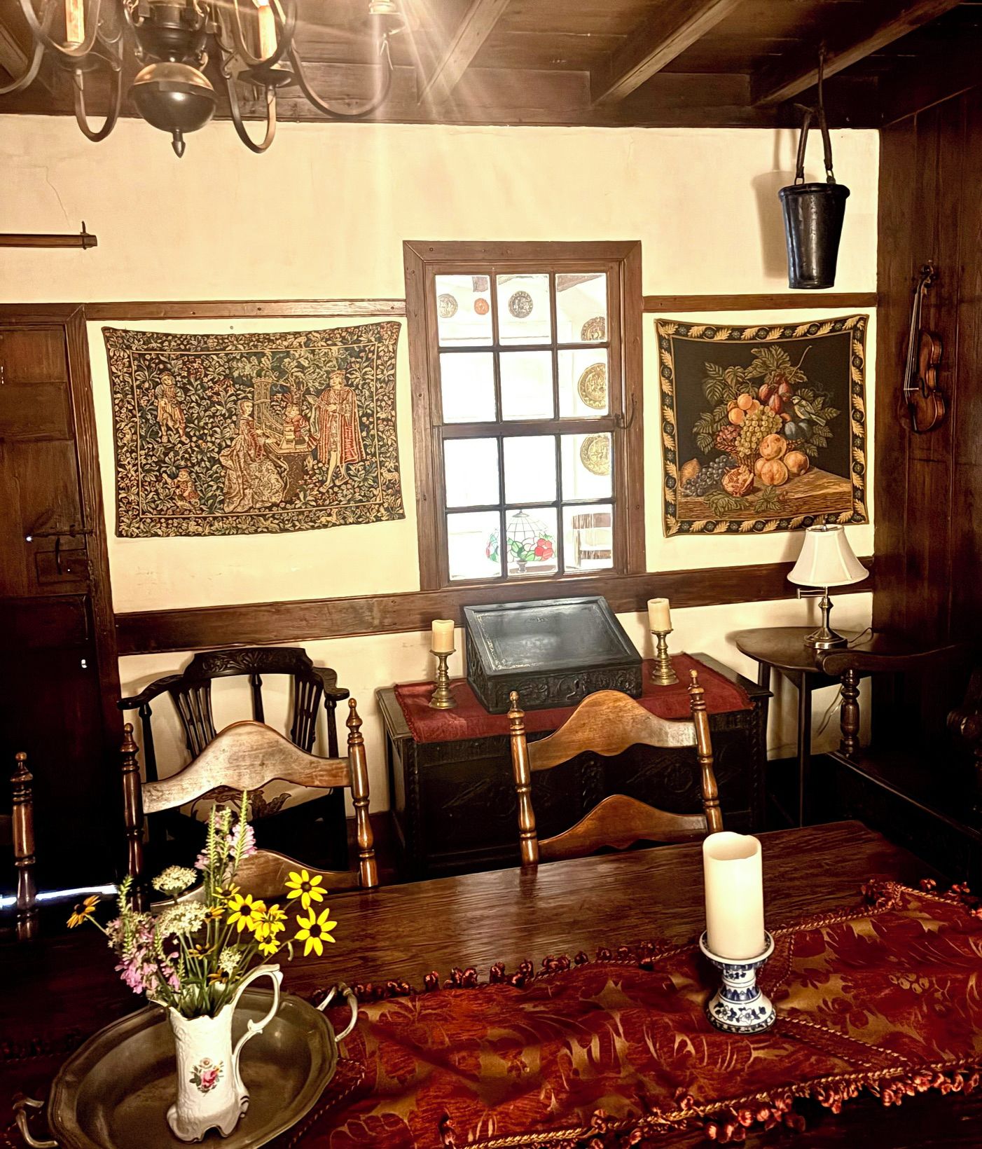 A room with a wooden table, a vase with flowers, a candle, and two framed pictures on the wall.
