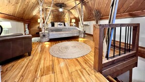 A cozy attic bedroom with a wooden ceiling, a large bed, a small table, and a chair. - Cedar Springs Cabin I Putting Green + Hot Tub (Hot Springs)