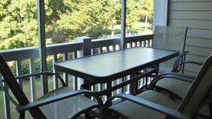 A covered patio with a glass table and metal chairs, overlooking a green landscape.
