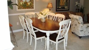 A dining area with a round table, white chairs, a vase of flowers, and two paintings on the wall.