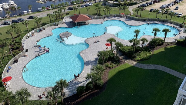 A large, multi-pond swimming area with a surrounding deck, palm trees, and a marina in the background.