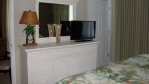 A hotel room with a white dresser, a television, a lamp, and a bed with a floral bedspread.