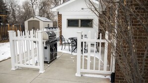 Un jardin avec un barbecue, un petit abri de jardin et une clôture blanche.