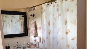 A bathroom with a white sink, dark cabinets, a mirror, and a shower curtain with a sea shell pattern. - Nestled on a hill with Mountain Views (Bo Cataño, Humacao)