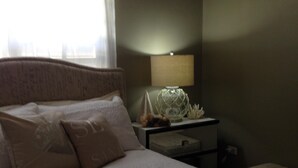 A neatly made bed with pillows, a bedside table with a lamp, and a nightstand with a decorative item. - Nestled on a hill with Mountain Views (Bo Cataño, Humacao)