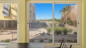 A room with a large sliding glass door leading to an outdoor garden area with a view of a building and palm trees.