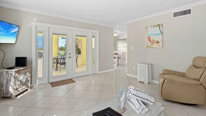 A spacious living area with a flat-screen TV, a beige leather recliner, and a dining area with a table and chairs.