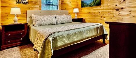 Un dormitorio de estilo cabaña con una cama, dos mesitas de noche, un aparador, una ventana con persianas y un cuadro en la pared.