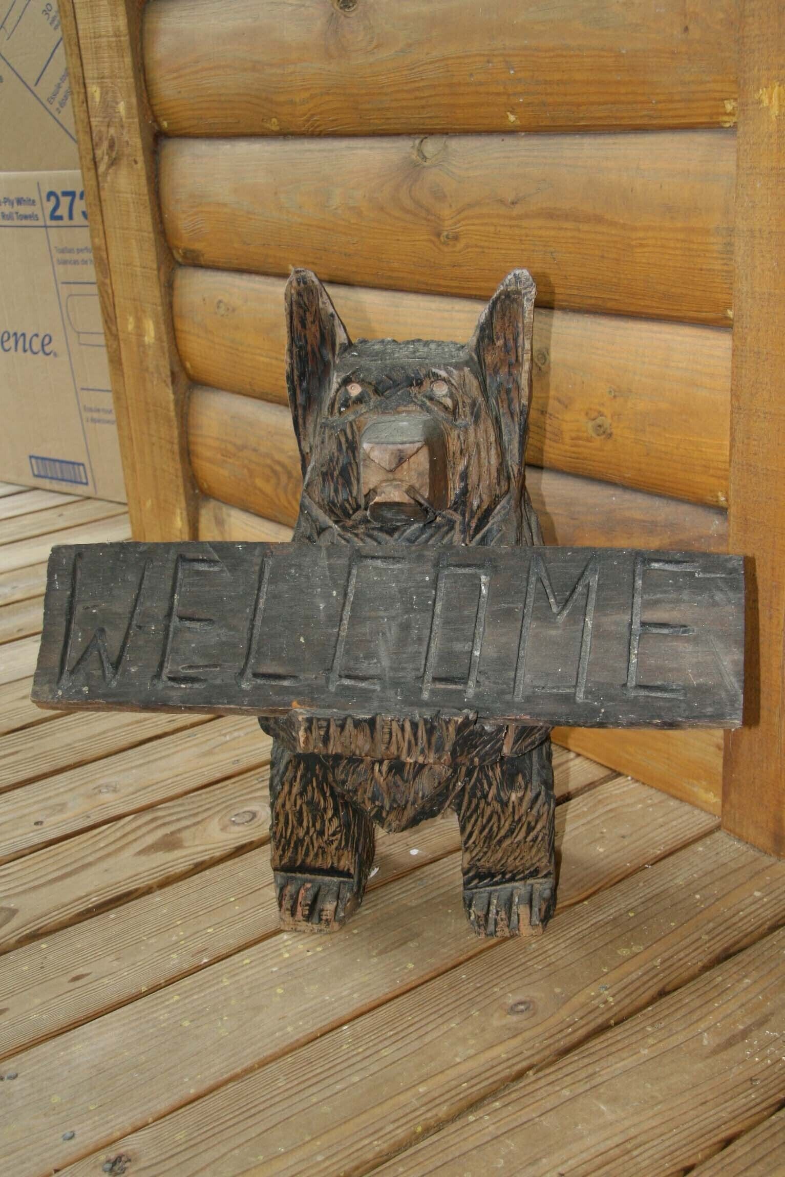 A wooden bear sculpture holding a sign that says "WELCOME".