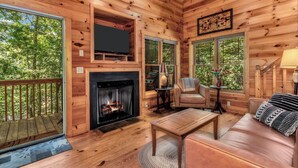 Een gezellig interieur van een chalet met een open haard, leren bank en een televisie erboven.
