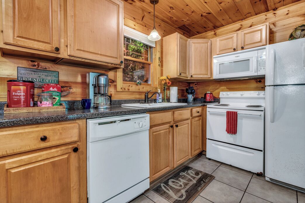 Una cocina con armarios de madera, lavavajillas blanco, estufa blanca y refrigerador blanco.