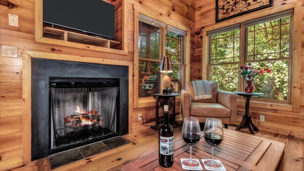 Een gezellig chaletinterieur met een open haard, houten wanden, een televisie en een tafel met wijnglazen en een fles wijn.