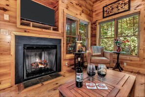 L’intérieur d’un chalet accueillant, avec une cheminée, des murs en bois, un téléviseur, une table avec des verres à vin et une bouteille.