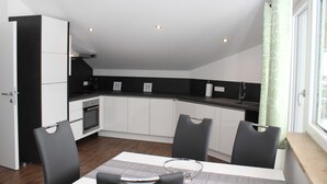 A modern kitchen with white cabinets, a black countertop, and a dining area with a table and chairs. - Apartment Lindpointner (Innerschwand am Mondsee)