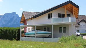 A two-story house with a balcony, a boat in the driveway, and mountains in the background. - Apartment Lindpointner (Innerschwand am Mondsee)