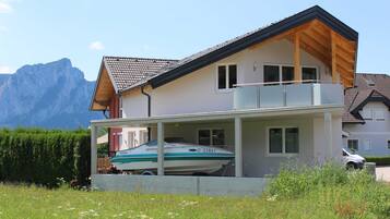 Ein zweigeschossiges Haus mit Balkon, einem Boot auf der Auffahrt und Bergen im Hintergrund.