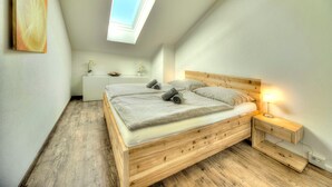 A bedroom with a wooden bed, bedside tables, a skylight, and a white wall. - Apartment Lindpointner (Innerschwand am Mondsee)