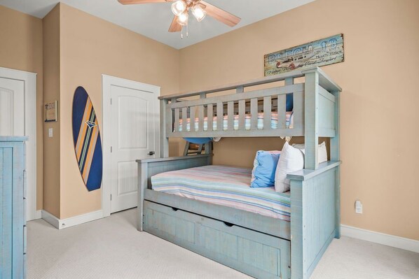 A bunk bed with striped bedding, a surfboard on the wall, and a vintage sign.