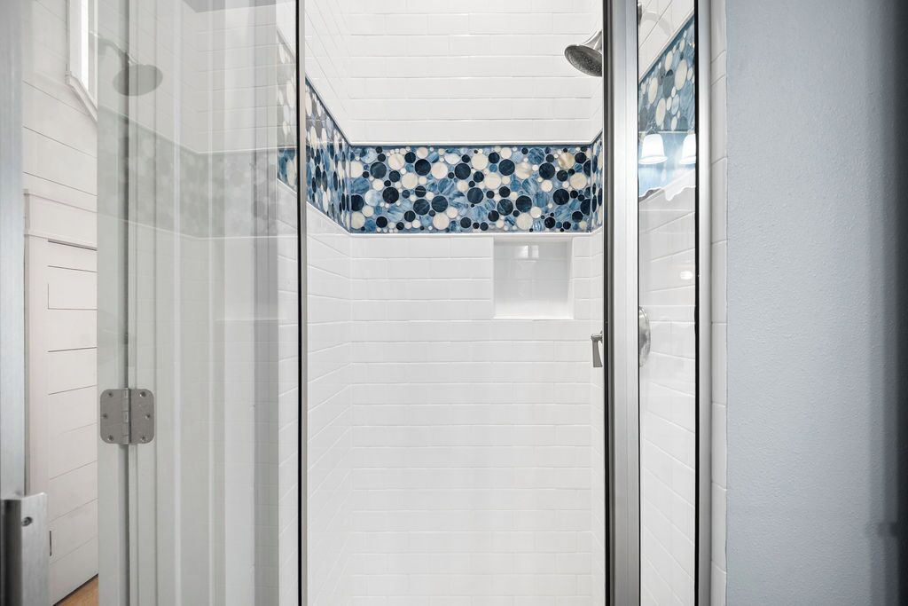 A narrow shower area with white tiled walls and a blue mosaic tile accent.